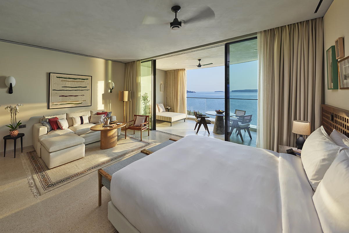 A beige bedroom with a floor to ceiling window sliding door to a terrace overlooking the sea