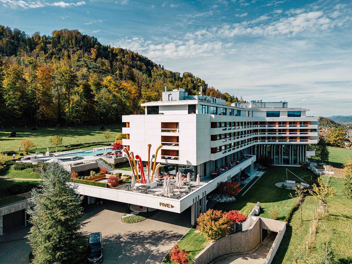 A white hotel building with an outdoor pool surrounded by grass and trees