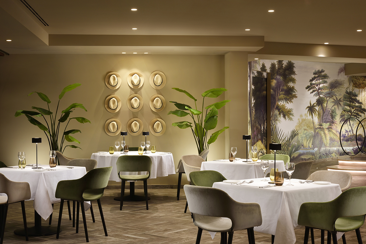 A restaurant with white table cloths, green chairs and plants around the room