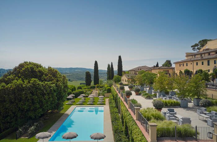 A swimming pool surrounded by a hotel trees and hills and fields