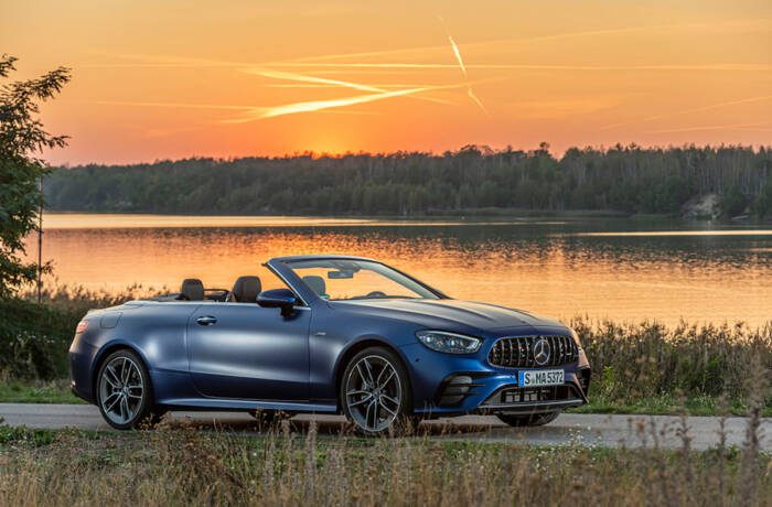 A blue car by a lake with an orange sunset