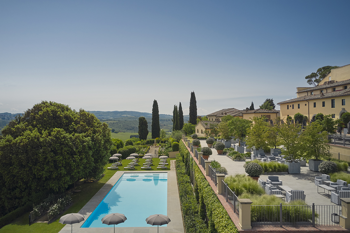 A swimming pool surrounded by a hotel trees and hills and fields