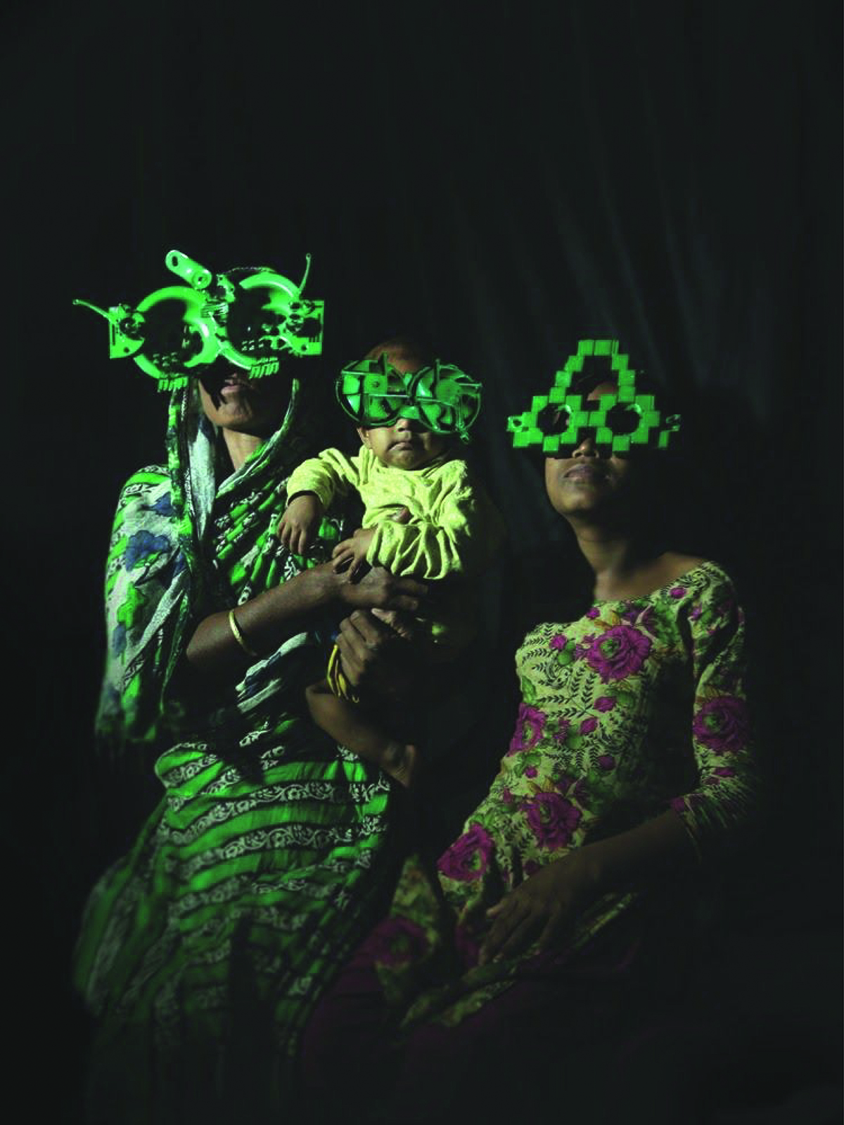 Two women, one holding a child in a dark room wearing large green glasses