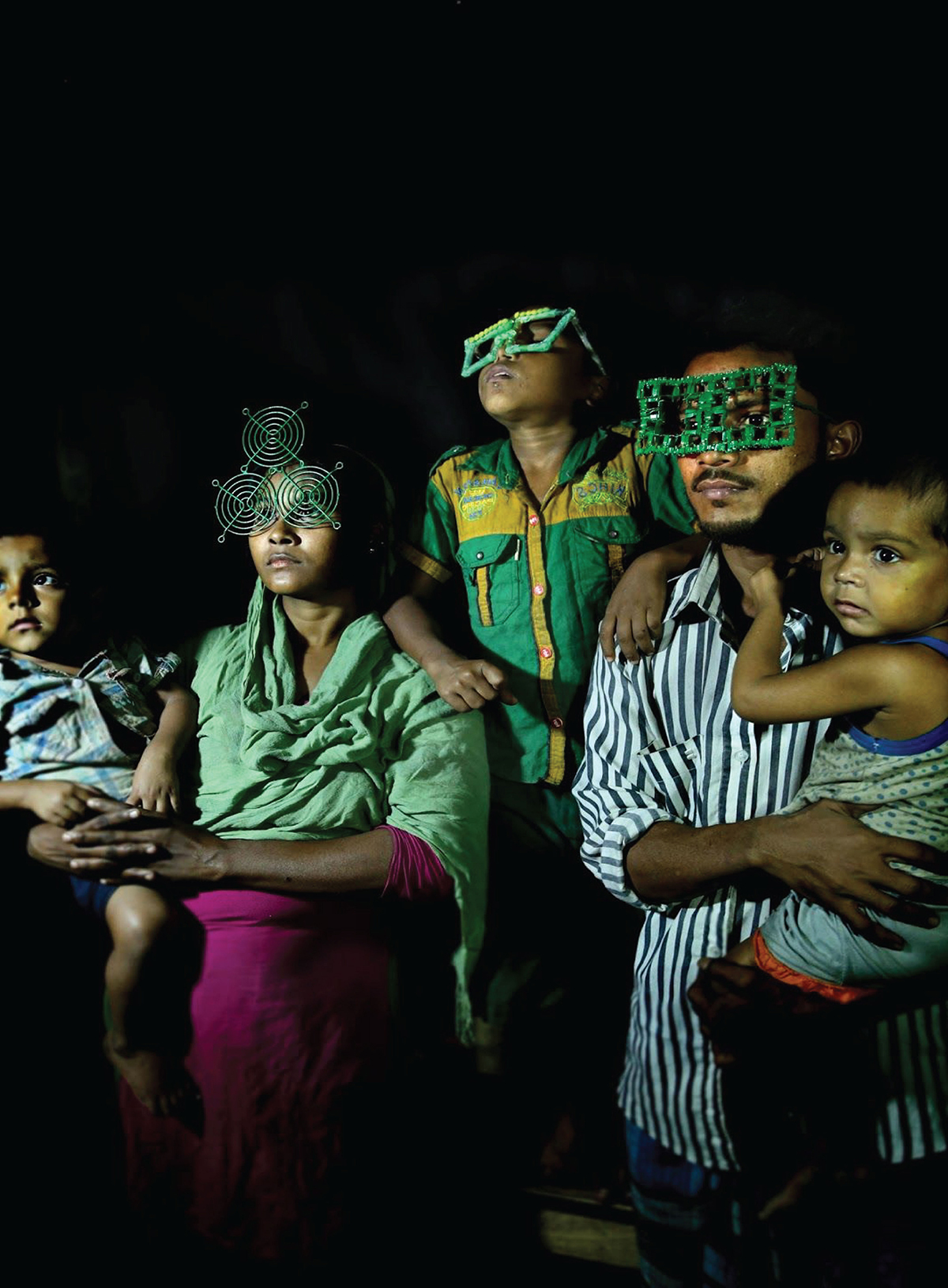 A family with children wearing large green glasses in a dark room