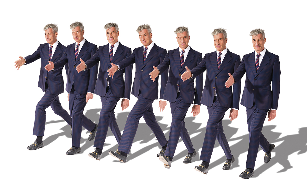 identical men in blue suits in a row with their arm our to shake a hand