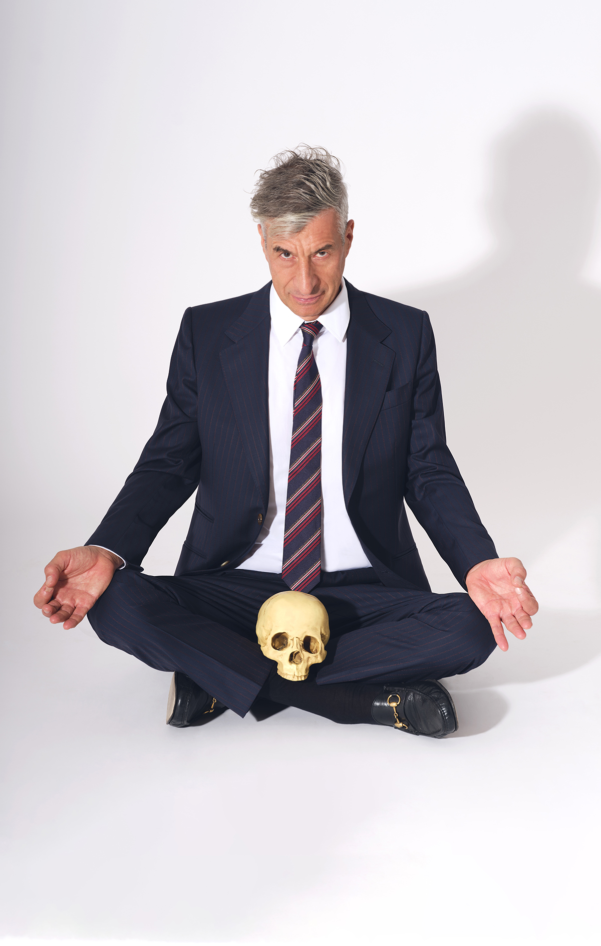 A man sitting cross legged with a skull in his lap wearing a suit