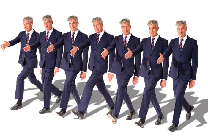 identical men in blue suits in a row with their arm our to shake a hand