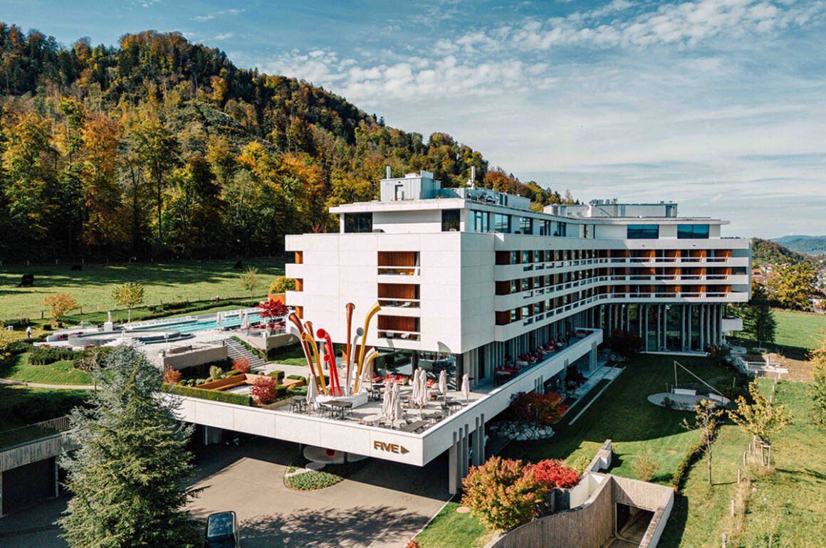 A white hotel building with an outdoor pool surrounded by grass and trees