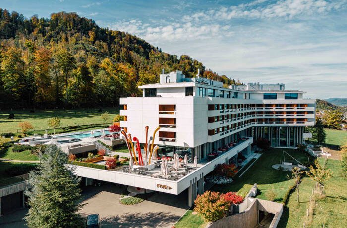 A white hotel building with an outdoor pool surrounded by grass and trees