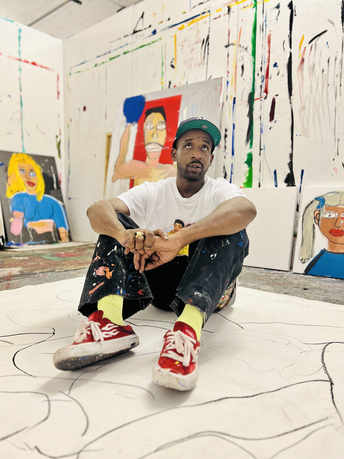 A man sitting on a drawing wearing red shoes, yellow socks, a green cap and white t-shirt with jeans