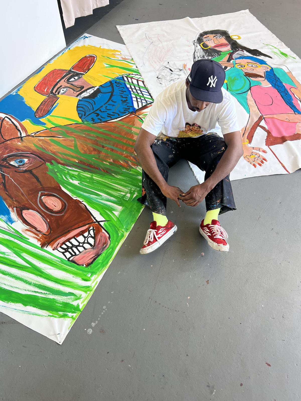 A man sitting on the floor surrounded by artworks
