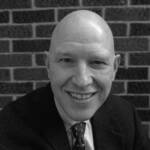 A bald man smiling wearing a suit and tie