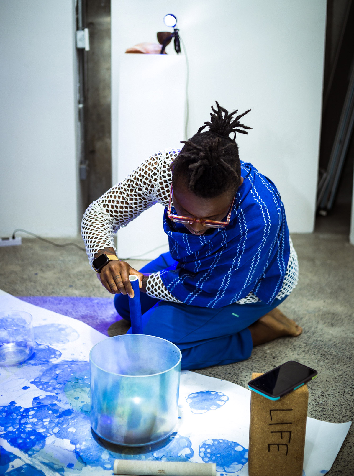 A woman wearing a white and blue top painting on the floor with blue paint 