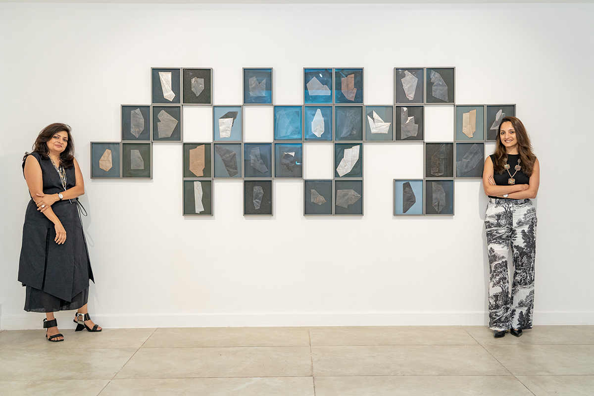 Two women standing on either side of frames hung on the walls of a gallery