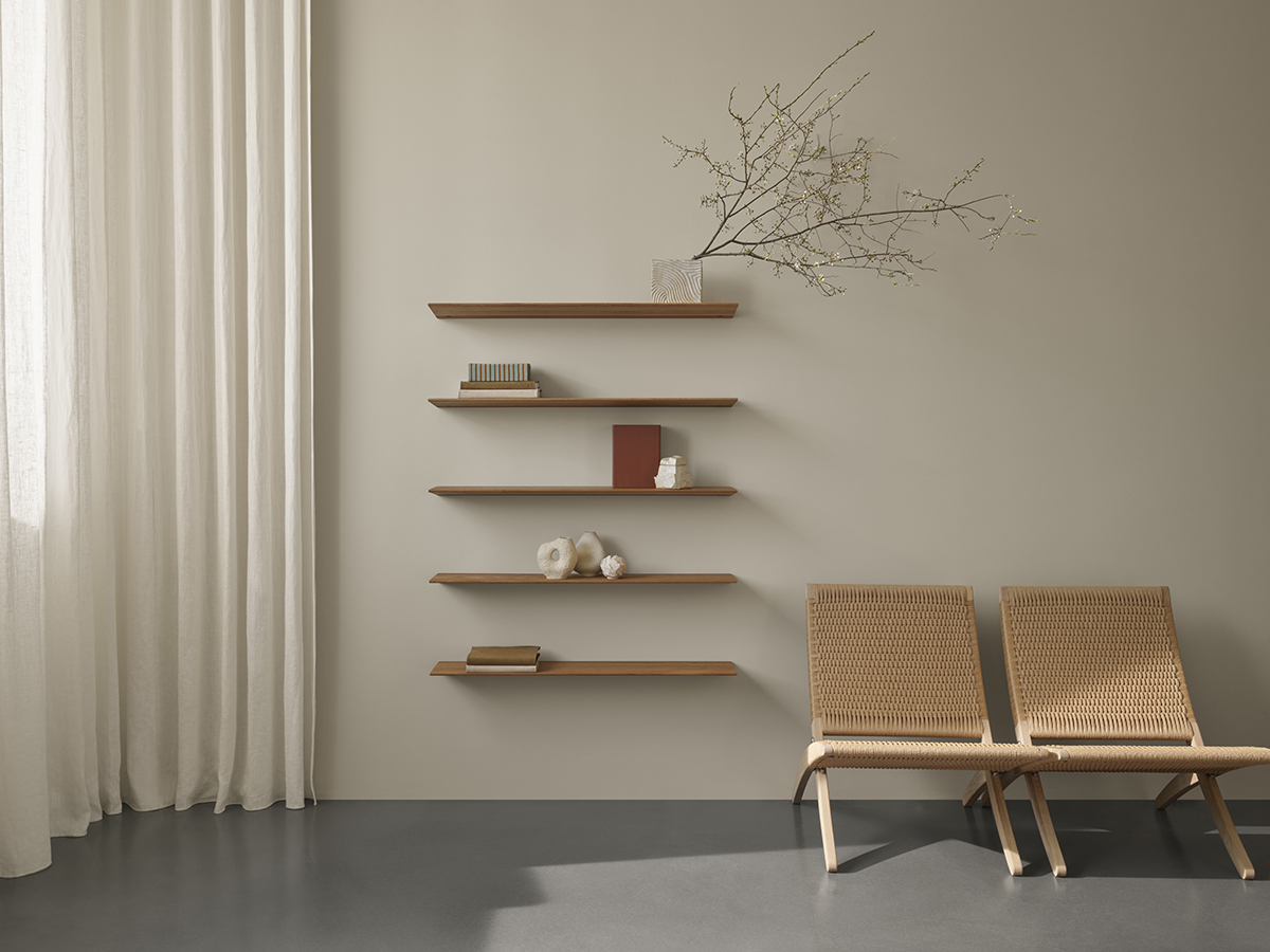 Simple wooden carl hansen shelves on a wall next to two brown chairs