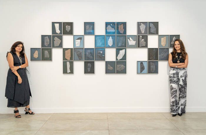 Two women standing on either side of frames hung on the walls of a gallery