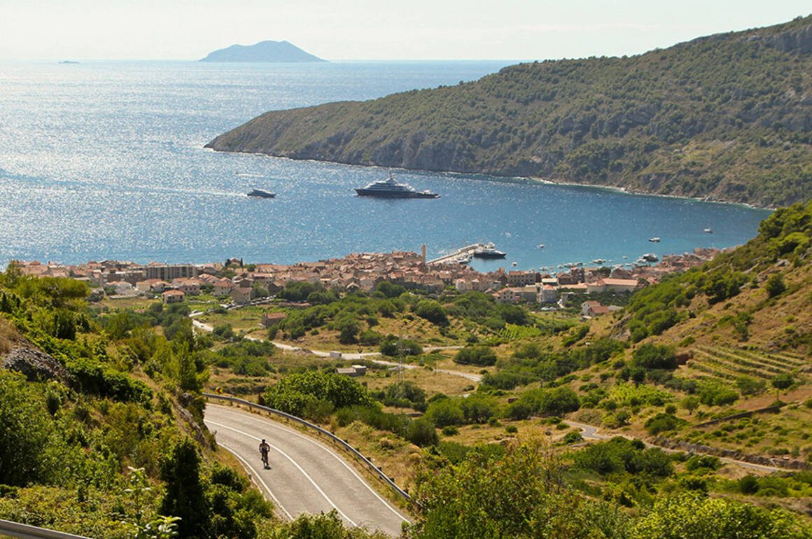 Birdseye view on blue ocean beside green land with a cyclist riding through the greenery