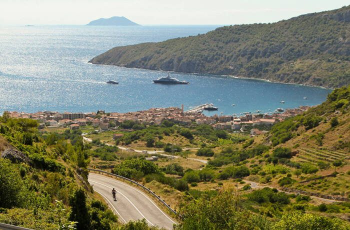 Birdseye view on blue ocean beside green land with a cyclist riding through the greenery