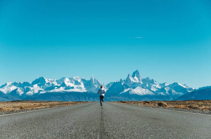 Person running down a road towards snowy mountains