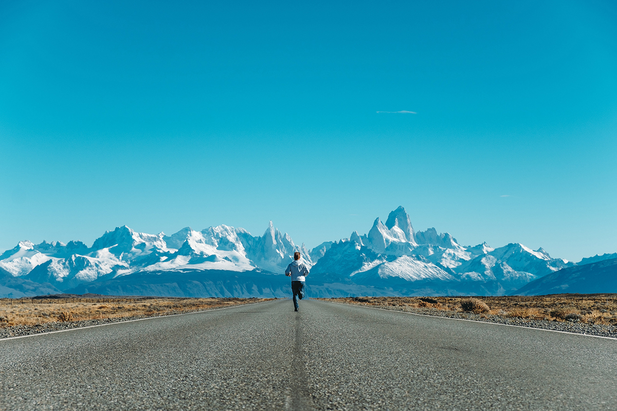 Person running down a road towards snowy mountains