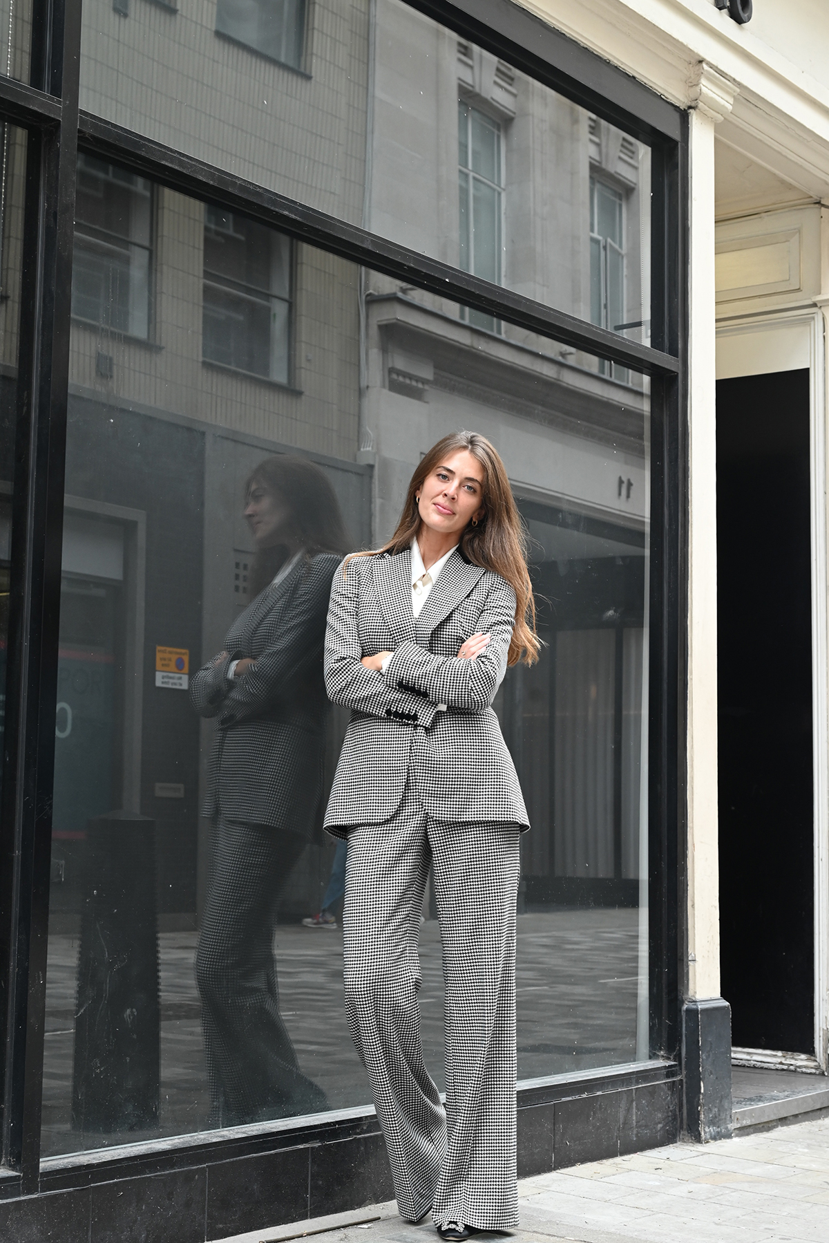 A girl standing in front of a large window wearing a grey striped suit