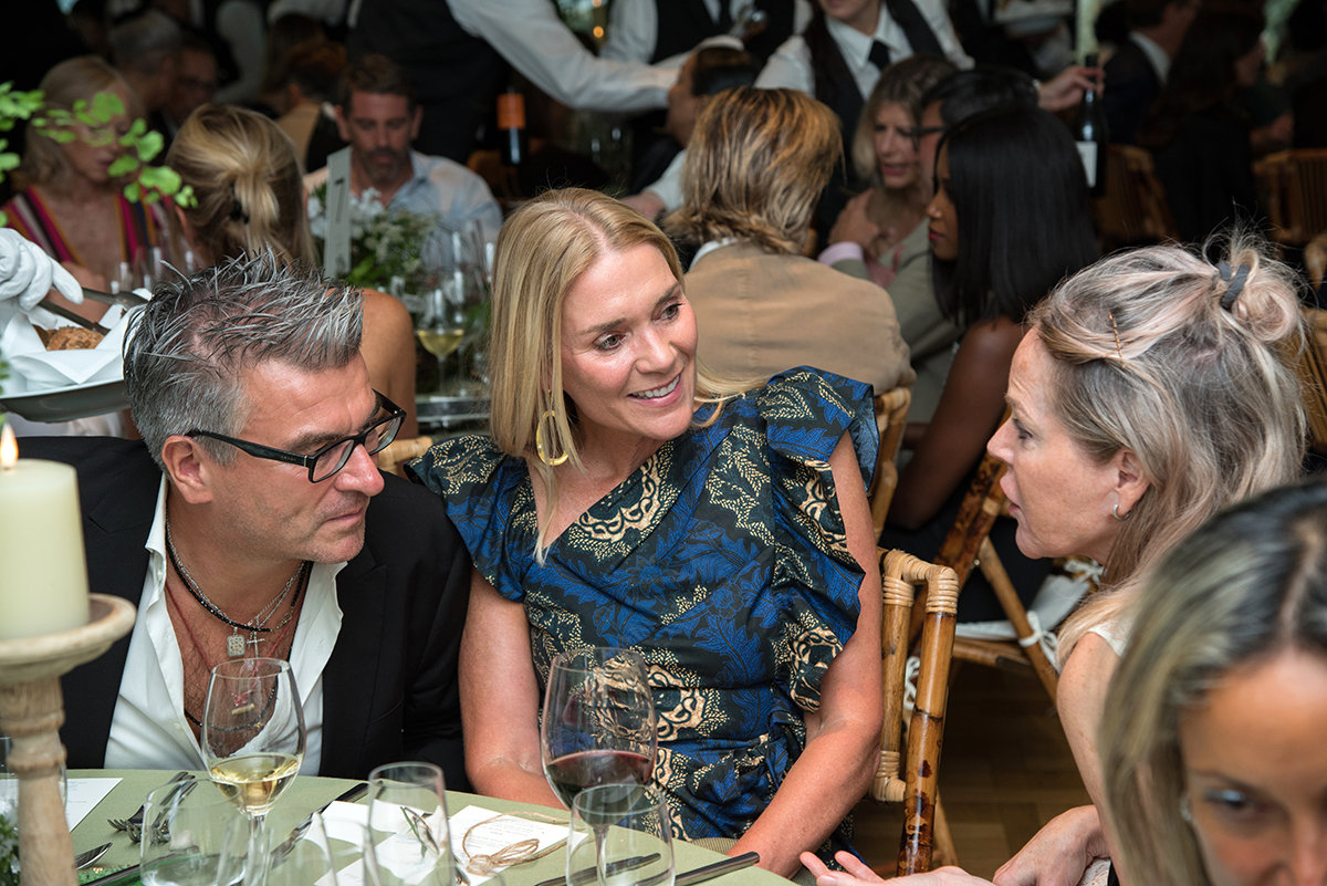 three people speaking at a table and the woman in the middle is wearing a blue dress