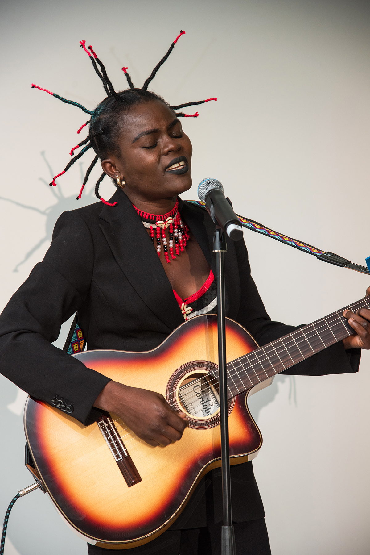 A woman playing the guitar with spiky red and black hair