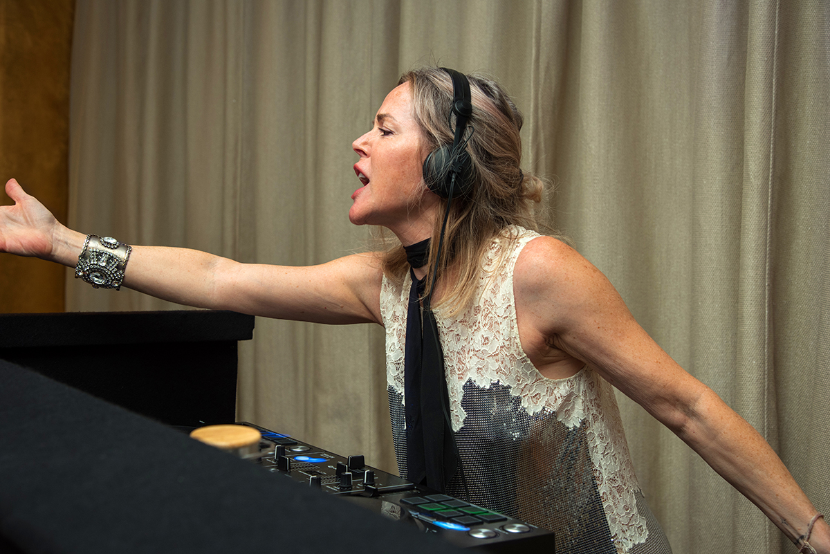 A woman DJ behind decks dancing with headphones on