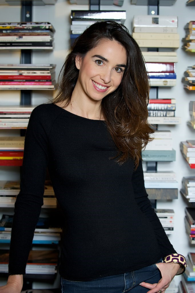 A brunette woman wearing a black top standing in front of books