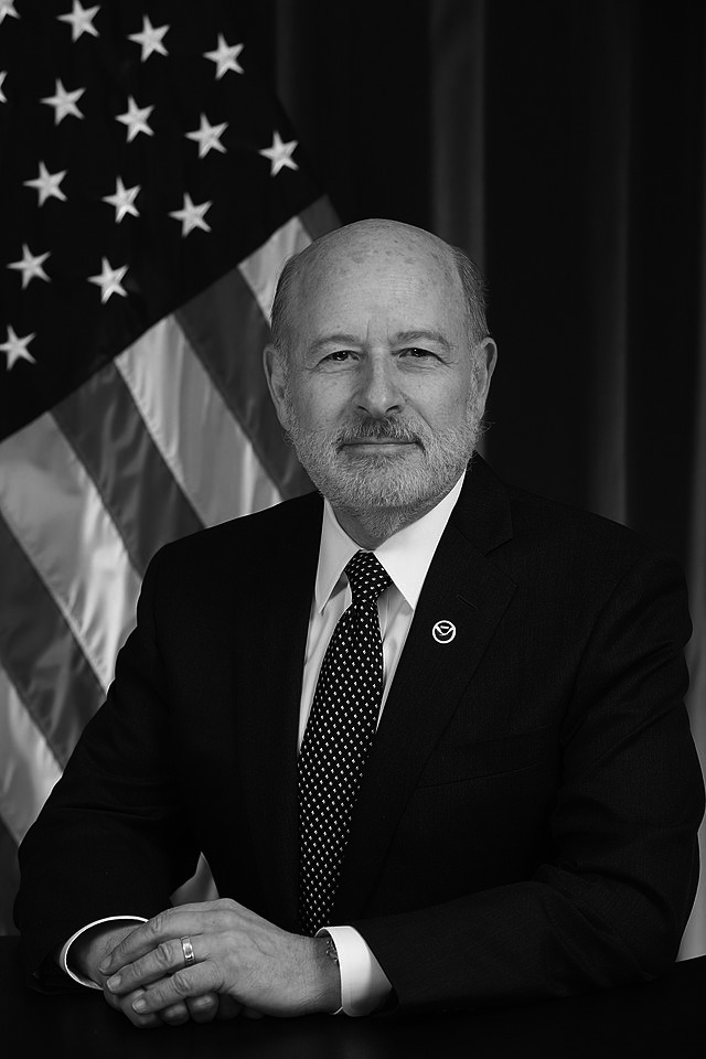 A man wearing a suit with an American flag behind him
