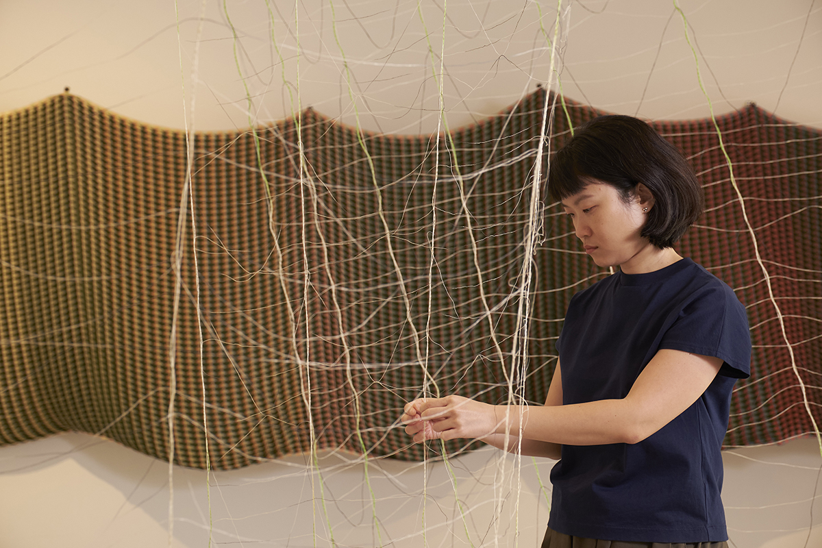 A woman playing with string on a tapestry hung on a wall