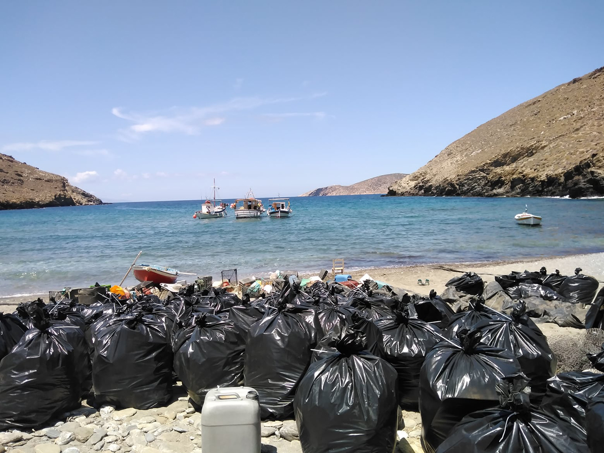 bin bags piled up with plastic on a beach facing the sea