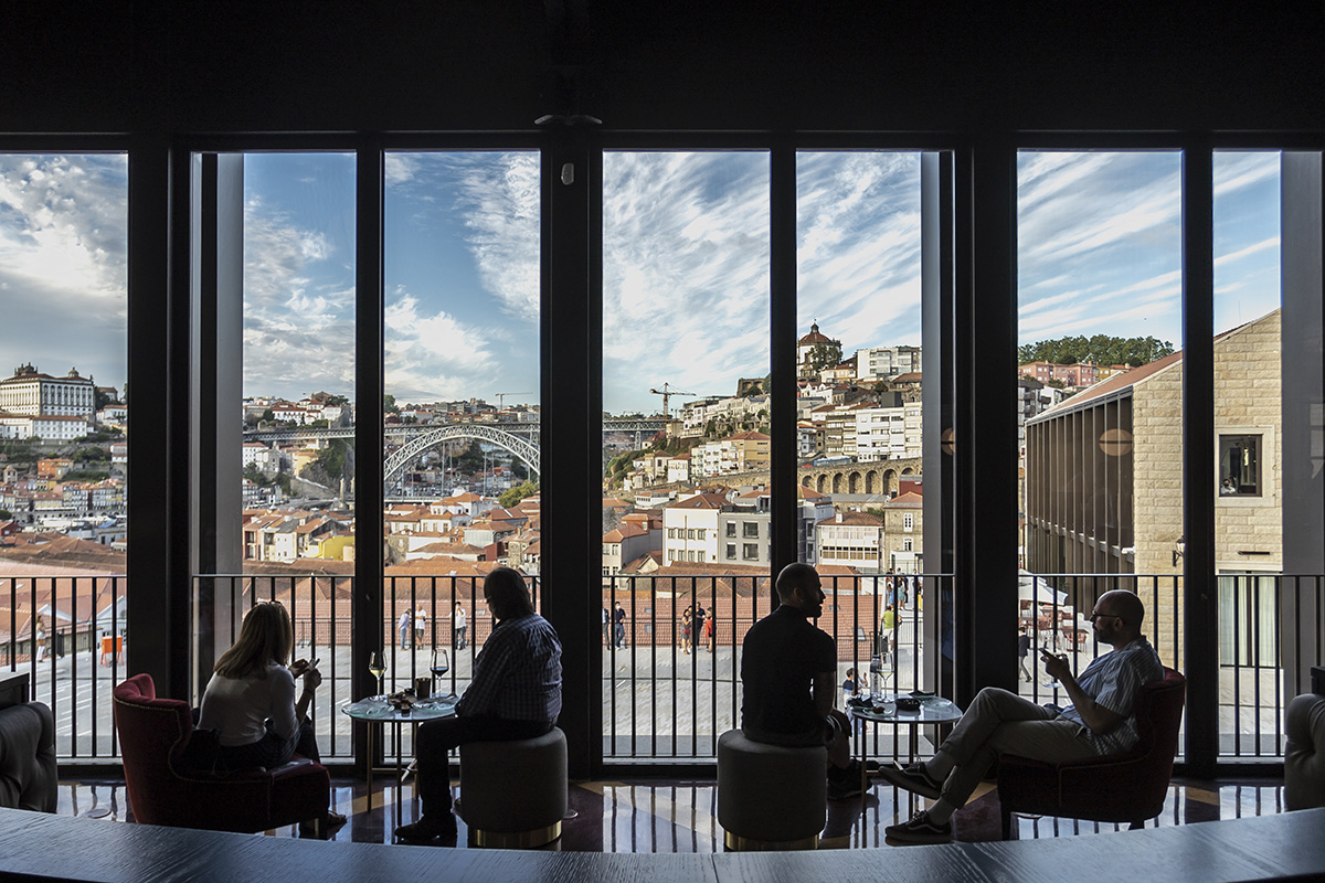 People sitting at tables in front of a large window overlooking a city