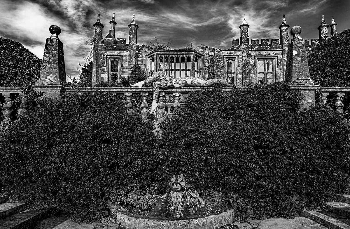 A black and white picture of a house and a woman lying on a balcony