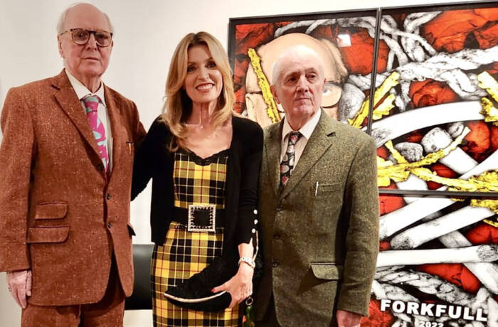 A woman wearing a black and yellow dress standing between two old men