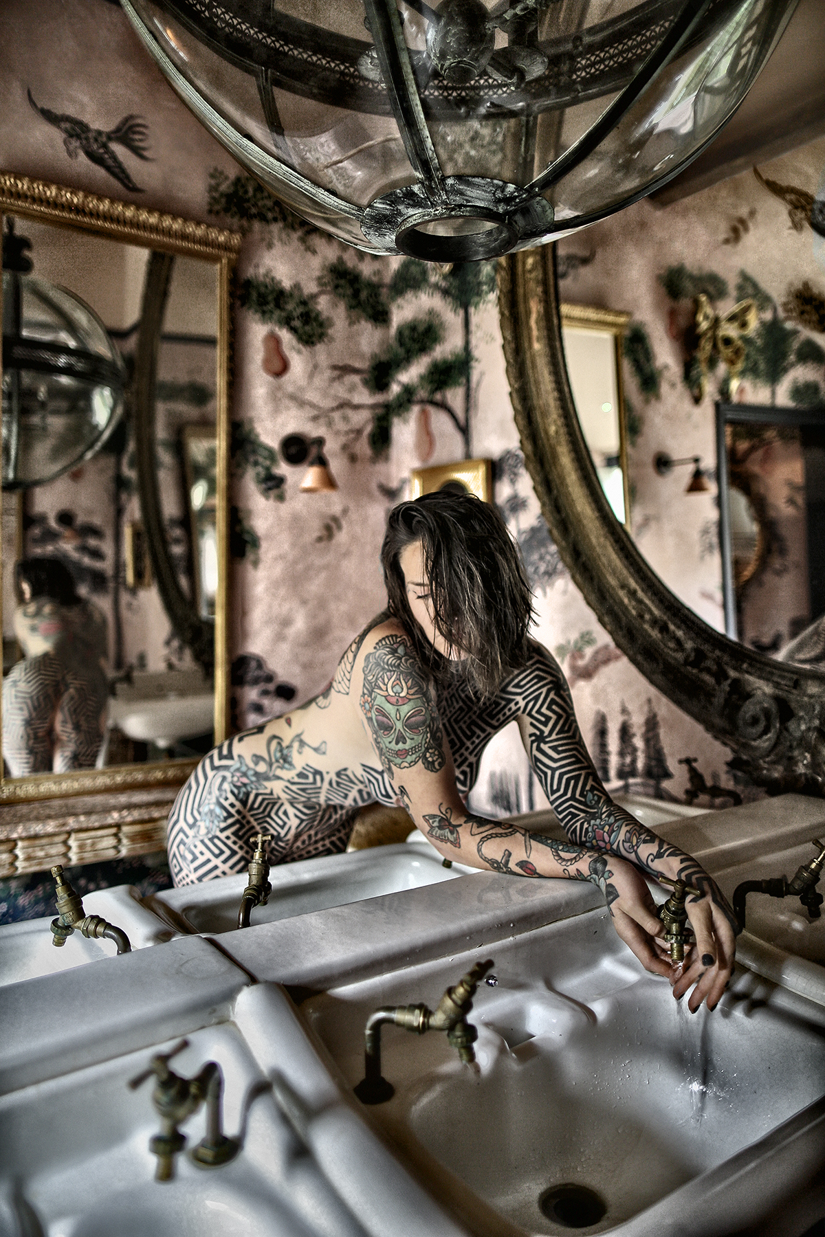 A woman covered in tattoos leaning on a bath with a mirror behind her