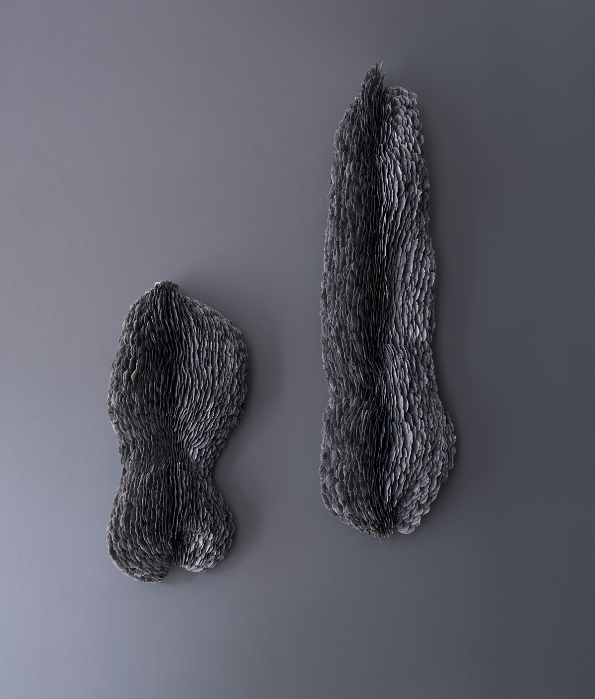 Two grey sculptures hung on a wall