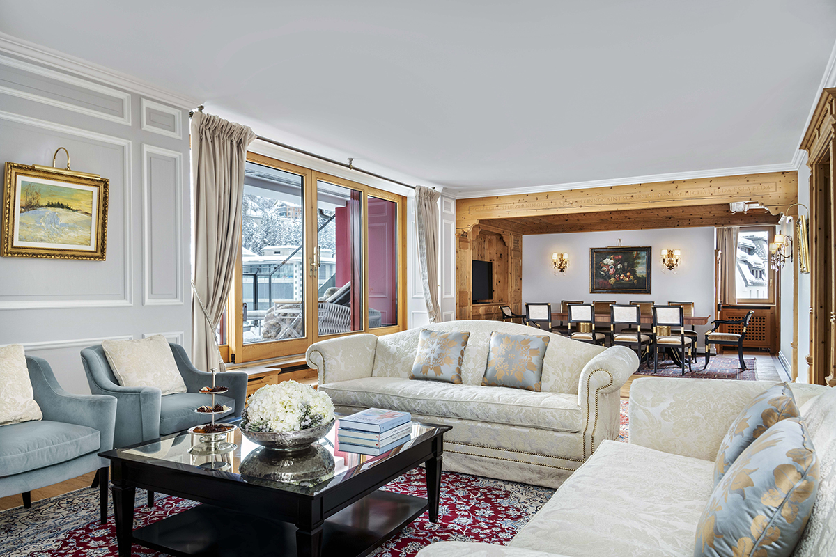 A living room with a long dining room table and chairs and cream couches with a black coffee table in the middle