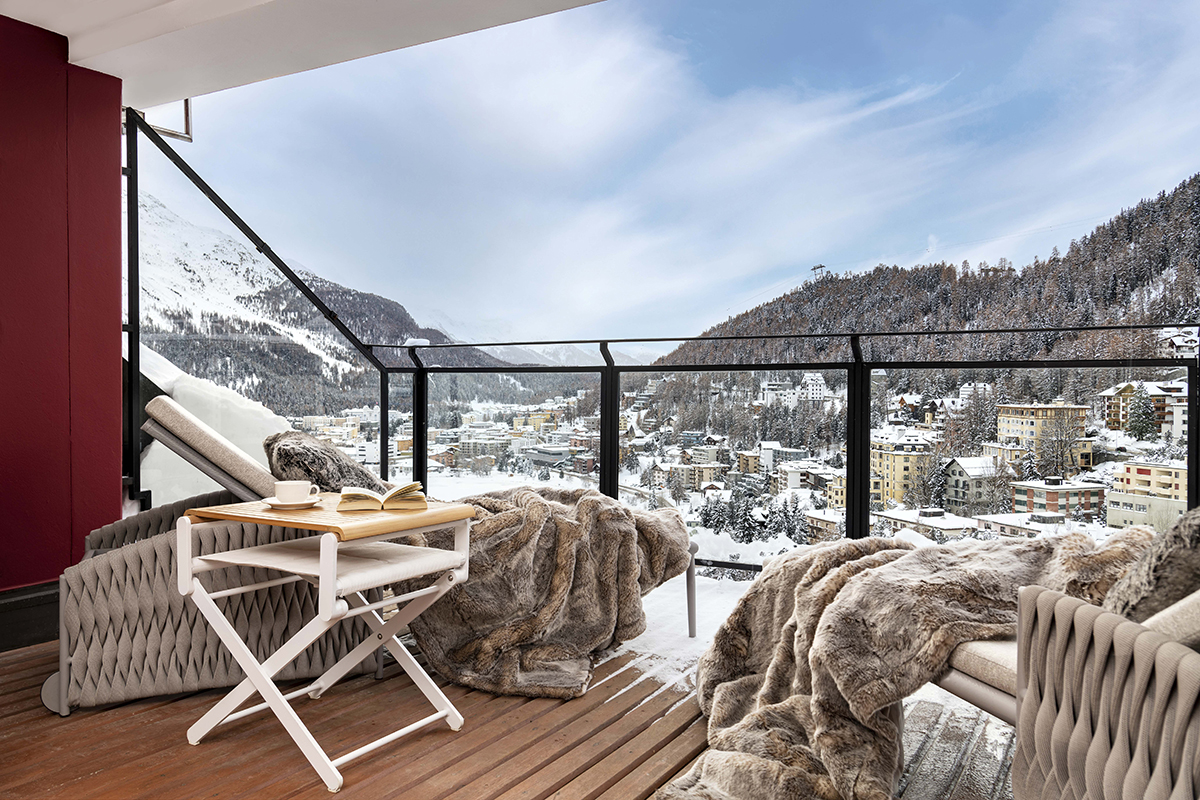 A terrace with chairs covered in fur blankets looking over snow covered mountains