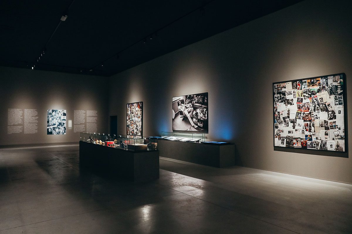 An exhibition room with photographs on the walls and objects in a glass box 