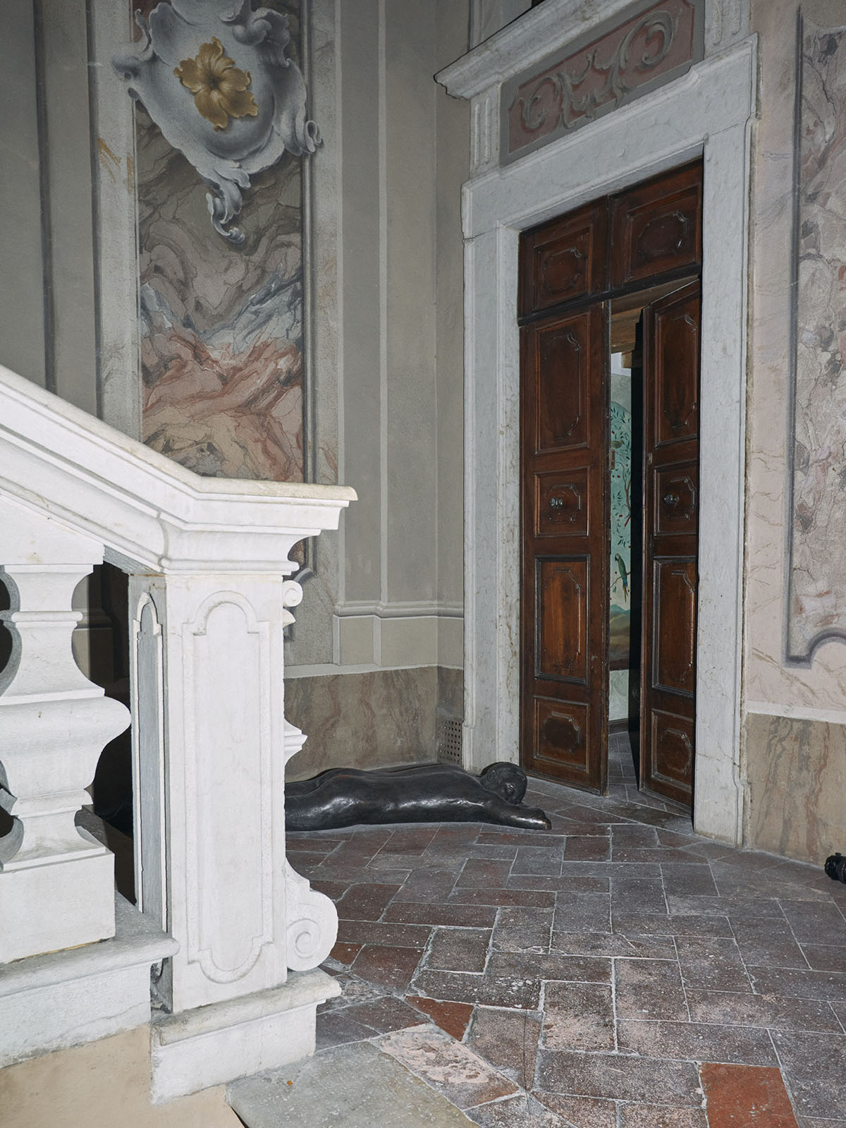 A white marble staircase in a hallway with painted walls and large wooden doors 