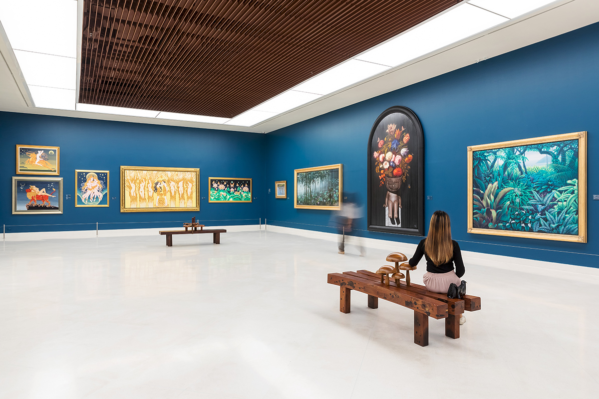 A blue room with paintings on the walls and benches in the middle of the room