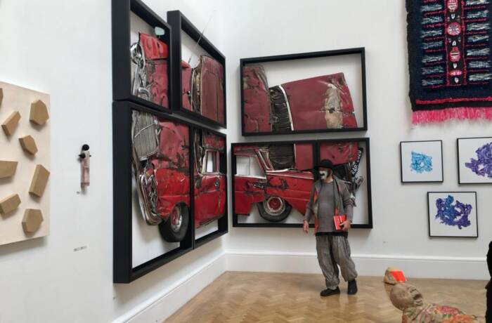 Man in a mask standing next to frames of a crushed car