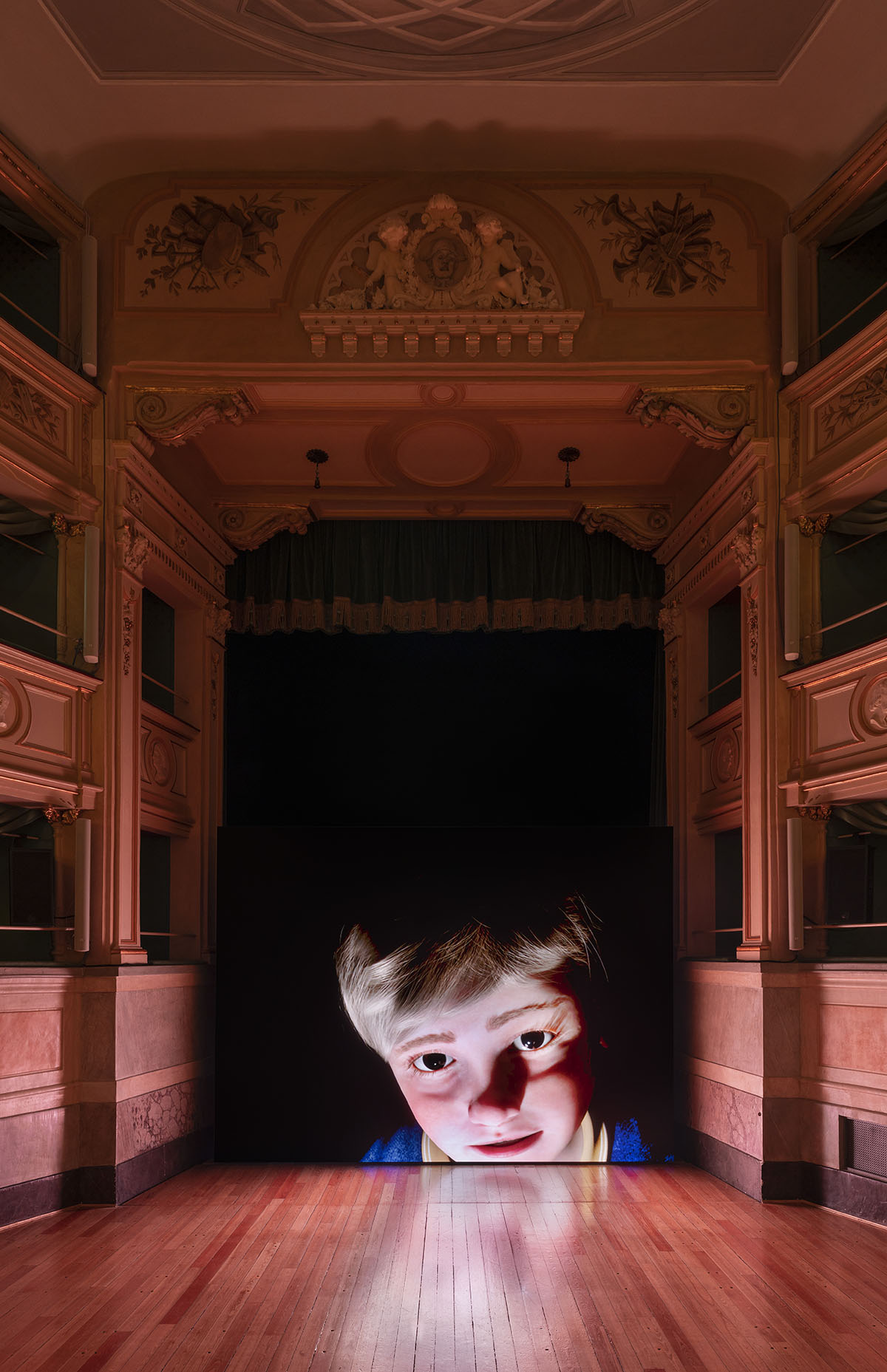 A theatre with a projection of a face of a boy on the stage curtain 