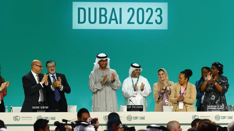 People standing behind a table on a stage with DUBAI 2023 written on a screen behind them
