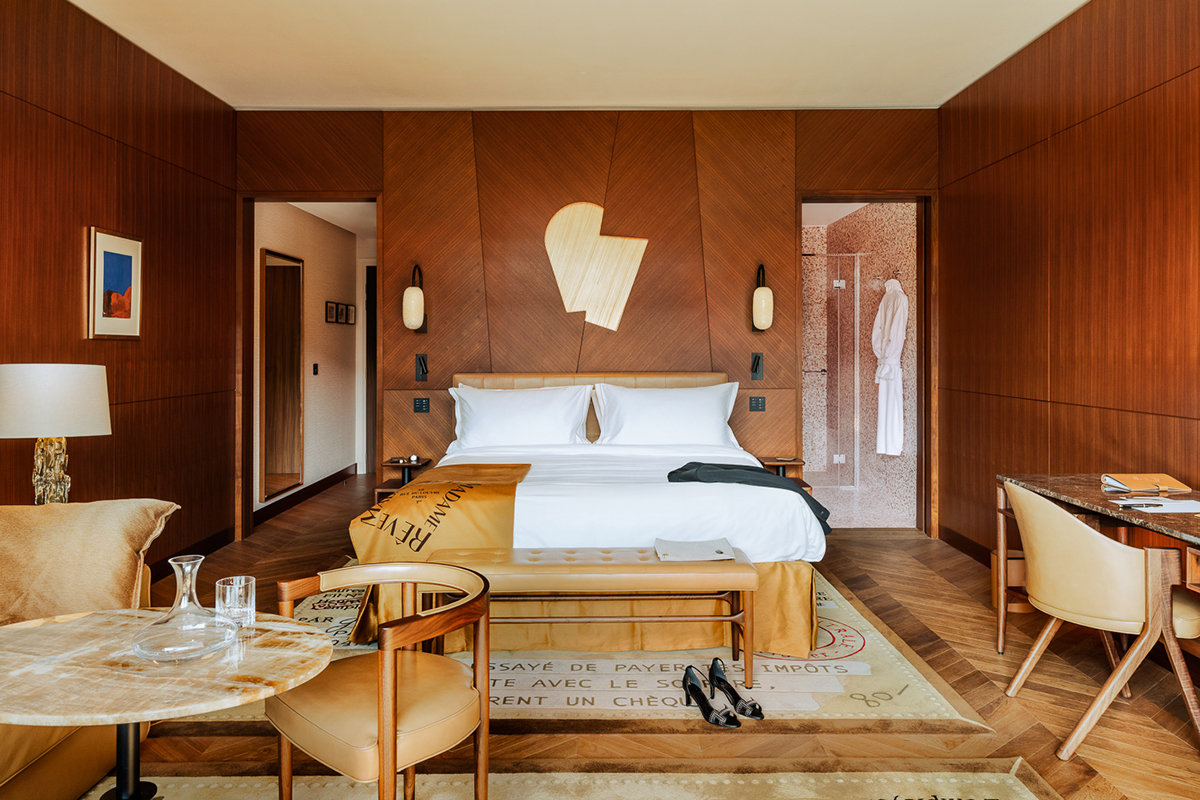 A bedroom with white pillows and duvets and beige wooden chairs, floors and walls