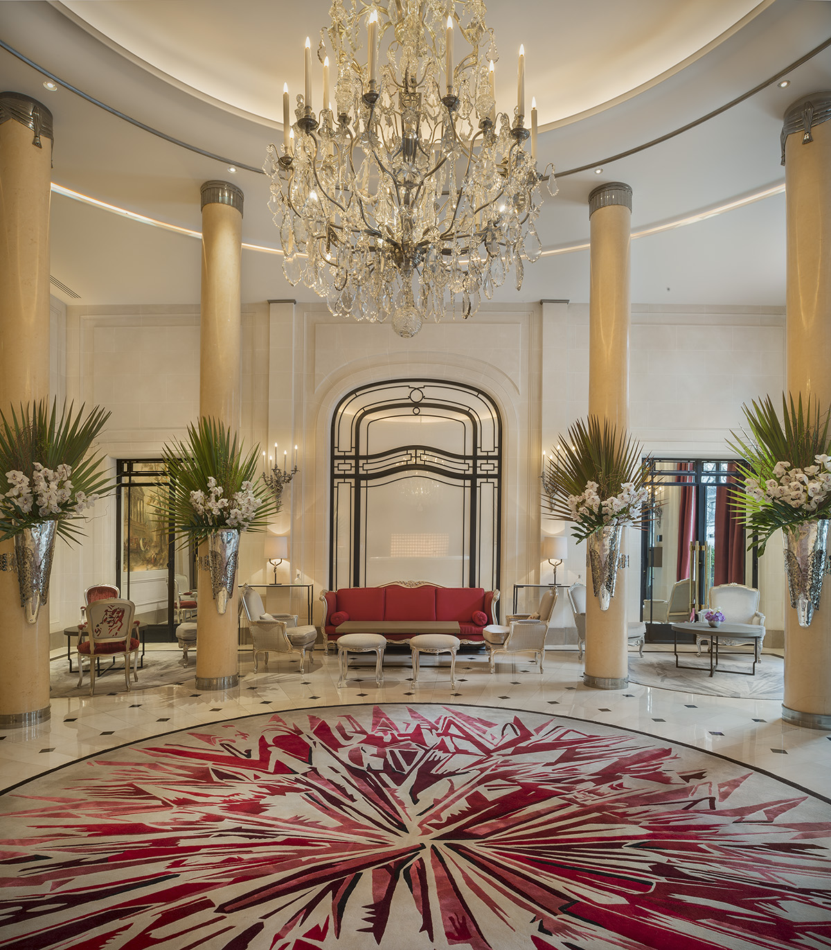 A red and white lobby with flowers hanging on pillars a large chandelier hanging over a rug