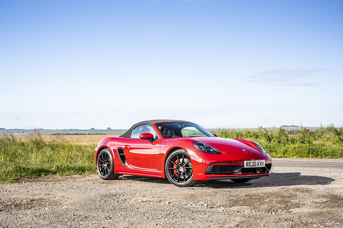 A red Porsche parked on the side of a road next to a field