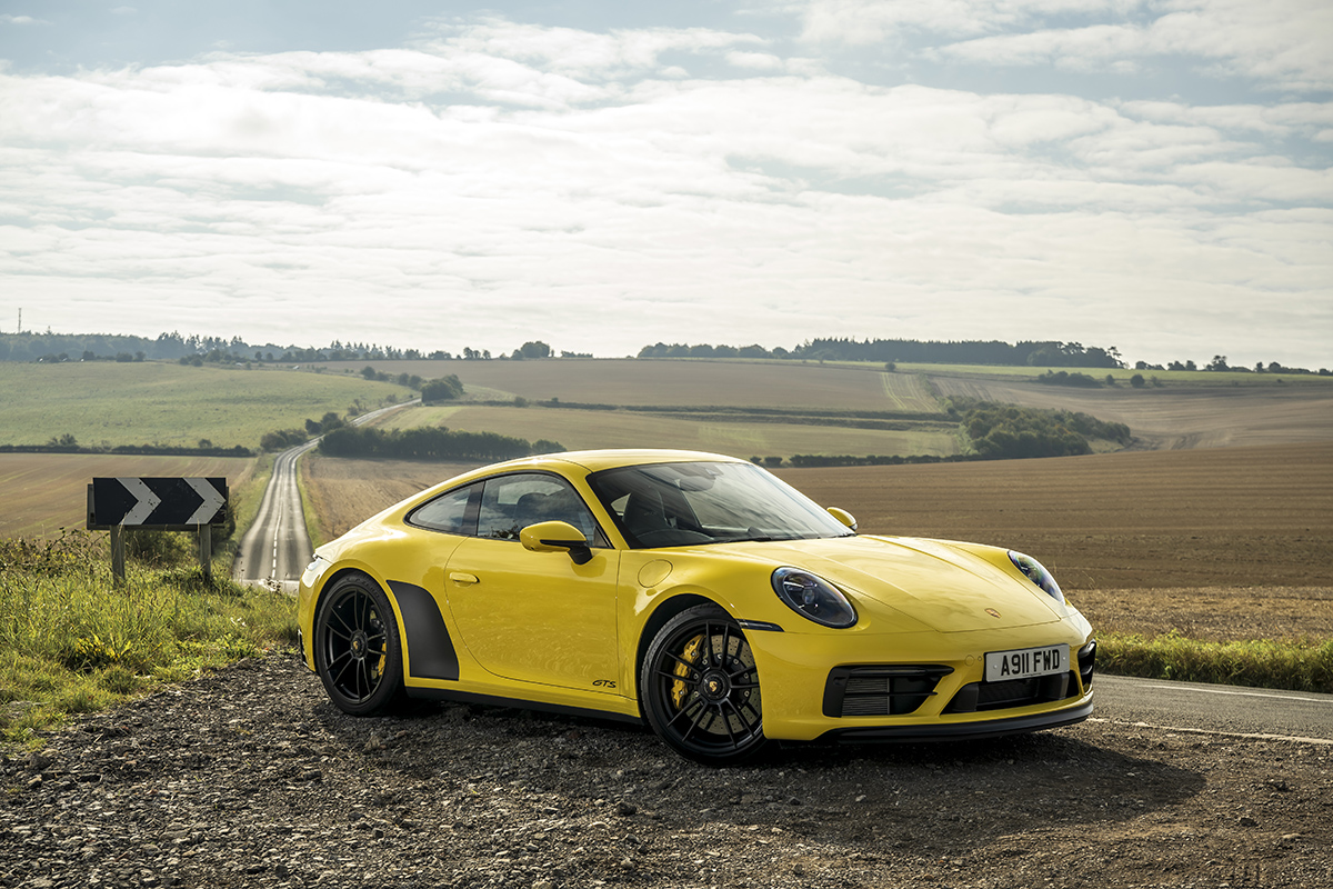 A yellow Porsche on a country road with fields in the background