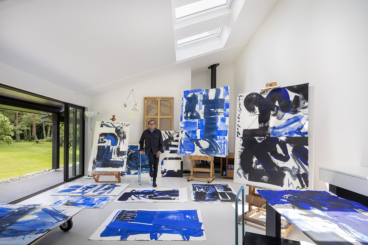 A man standing amongst blue paintings in a studio